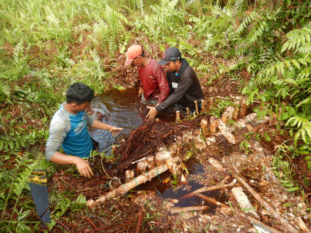 KMP men wading in water building small canal dam